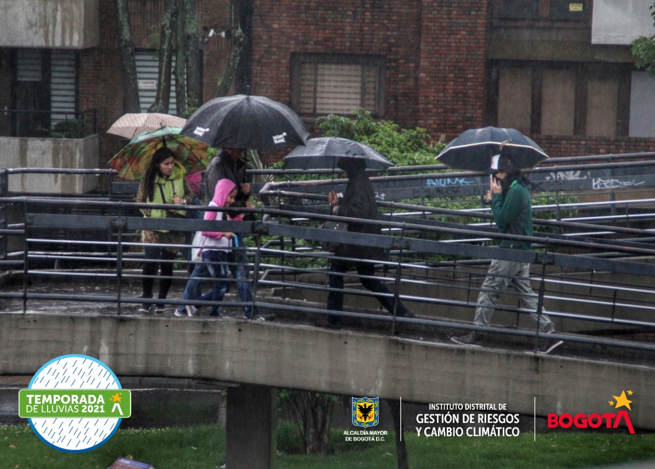 Personas pasando por un puente peatonal con sombrilla